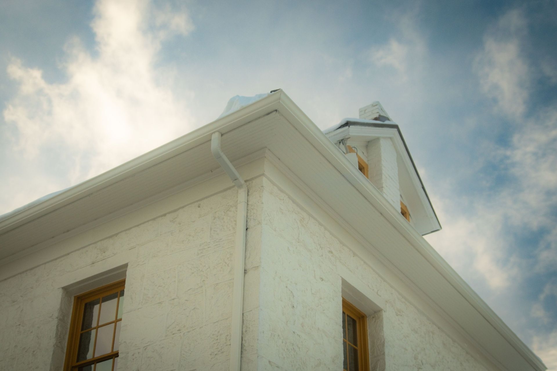 A vintage house with an elegant gable roof viewed from below against a partially cloudy sky.